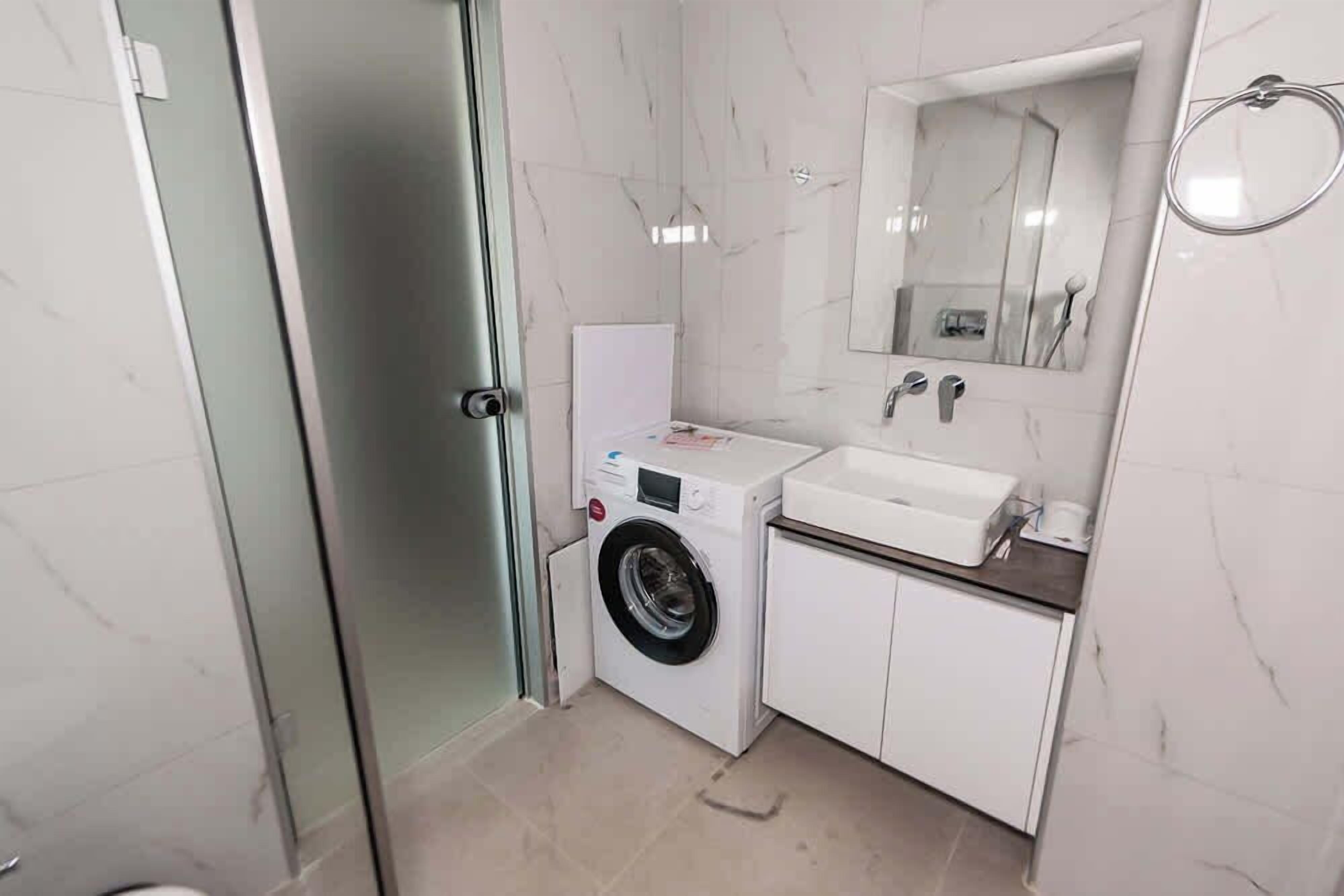 A compact bathroom with a washing machine, a sink, and a mirror.