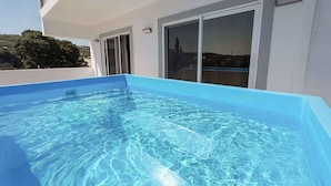 A rectangular swimming pool with clear blue water, surrounded by a white building with large windows and a door.