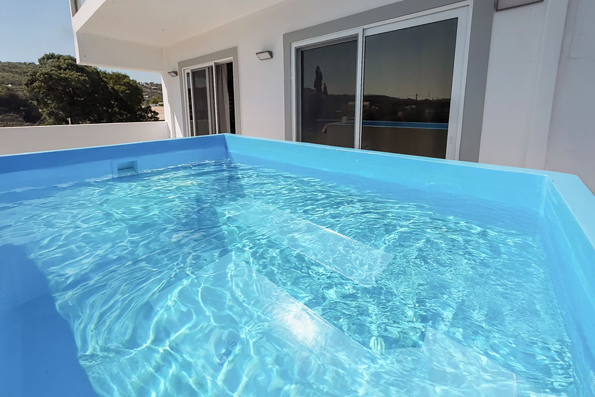 A rectangular swimming pool with clear blue water, surrounded by a white building with large windows and a door.
