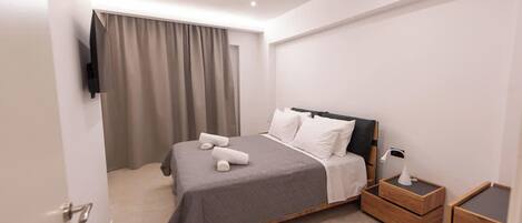 Ein modernes Hotelzimmer mit einem Bett, einem Nachttisch mit Lampe und einem an der Wand befestigten Fernseher.