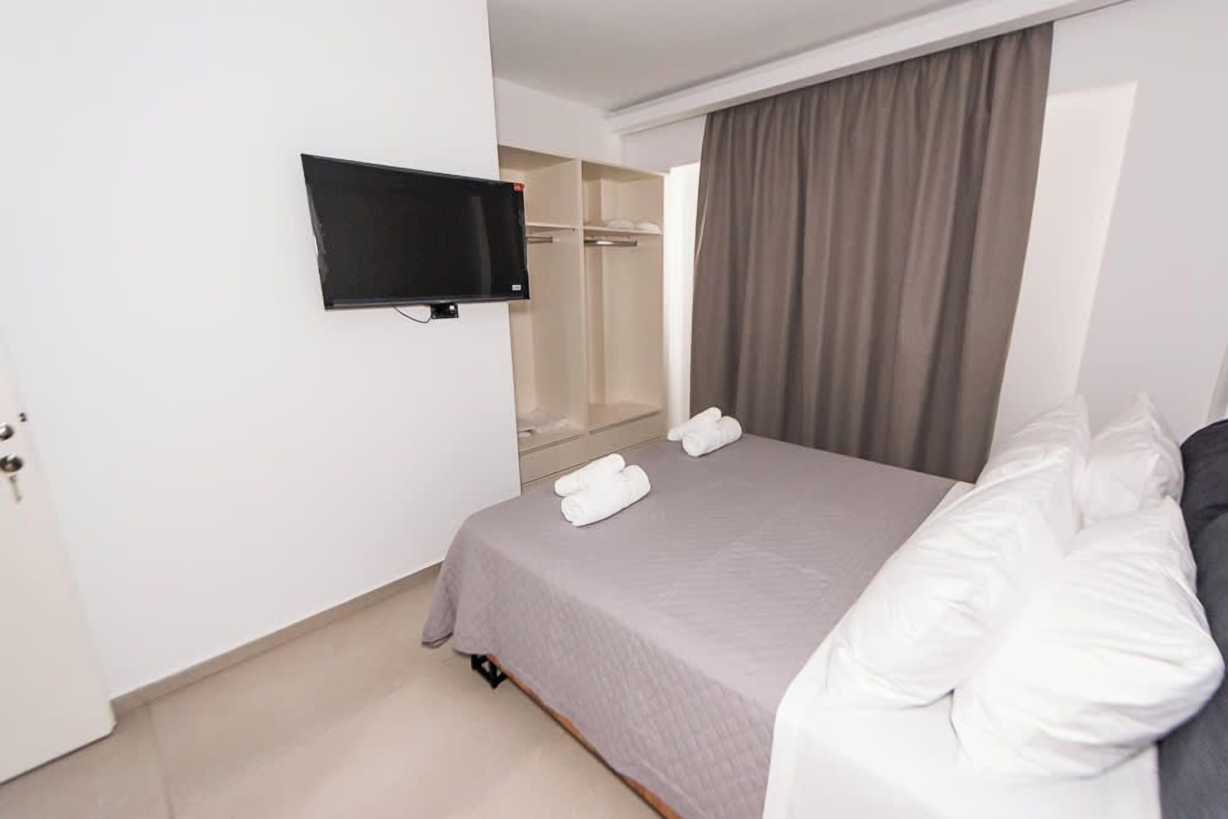 Ein Hotelzimmer mit Bett, Wandfernseher, begehbarer Kleiderschrank und einem Fenster mit Vorhängen.