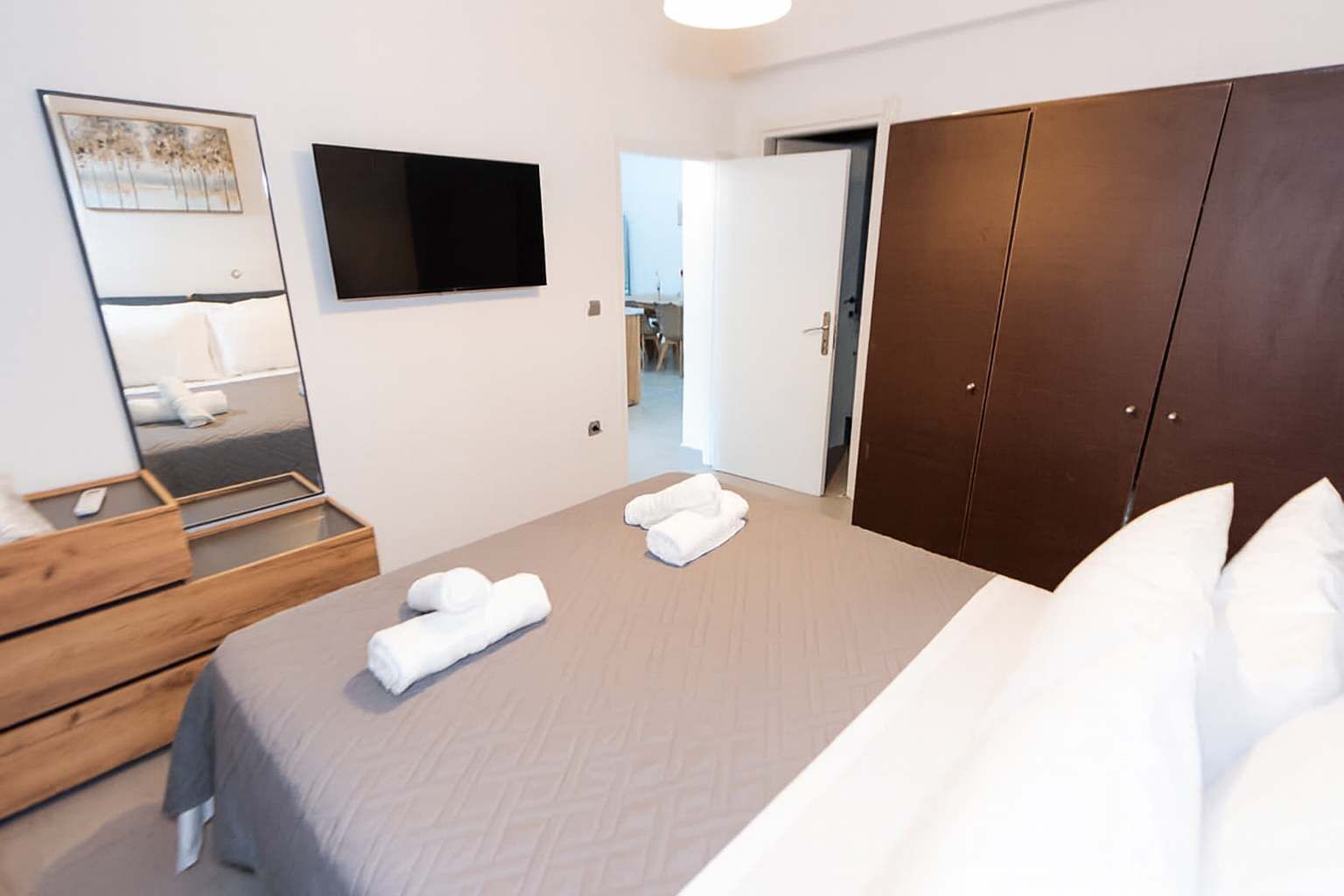 Ett modernt hotellrum med en stor säng, en byrå i trä, en platt-TV och en garderob.