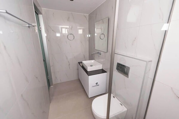 A modern bathroom with a glass-enclosed shower, a white sink with a black countertop, and a toilet.