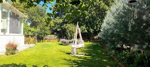 A well-maintained garden with a hanging chair, a white building with large windows, and a variety of trees and shrubs.