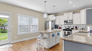 A modern kitchen with white cabinets, a central island with bar stools, stainless steel appliances, and pendant lighting.