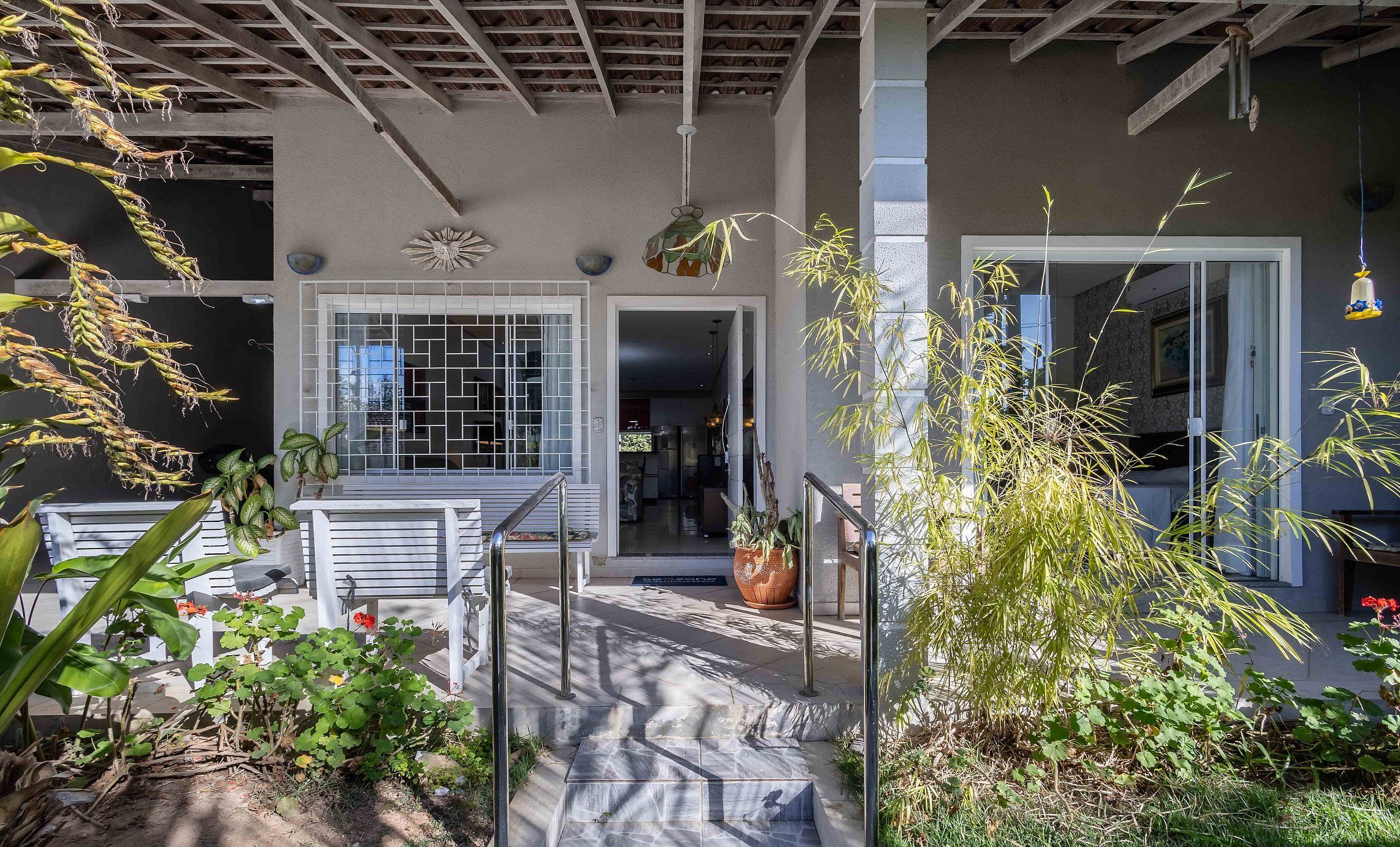 A covered outdoor area with a bench, potted plants, and a view into the house.