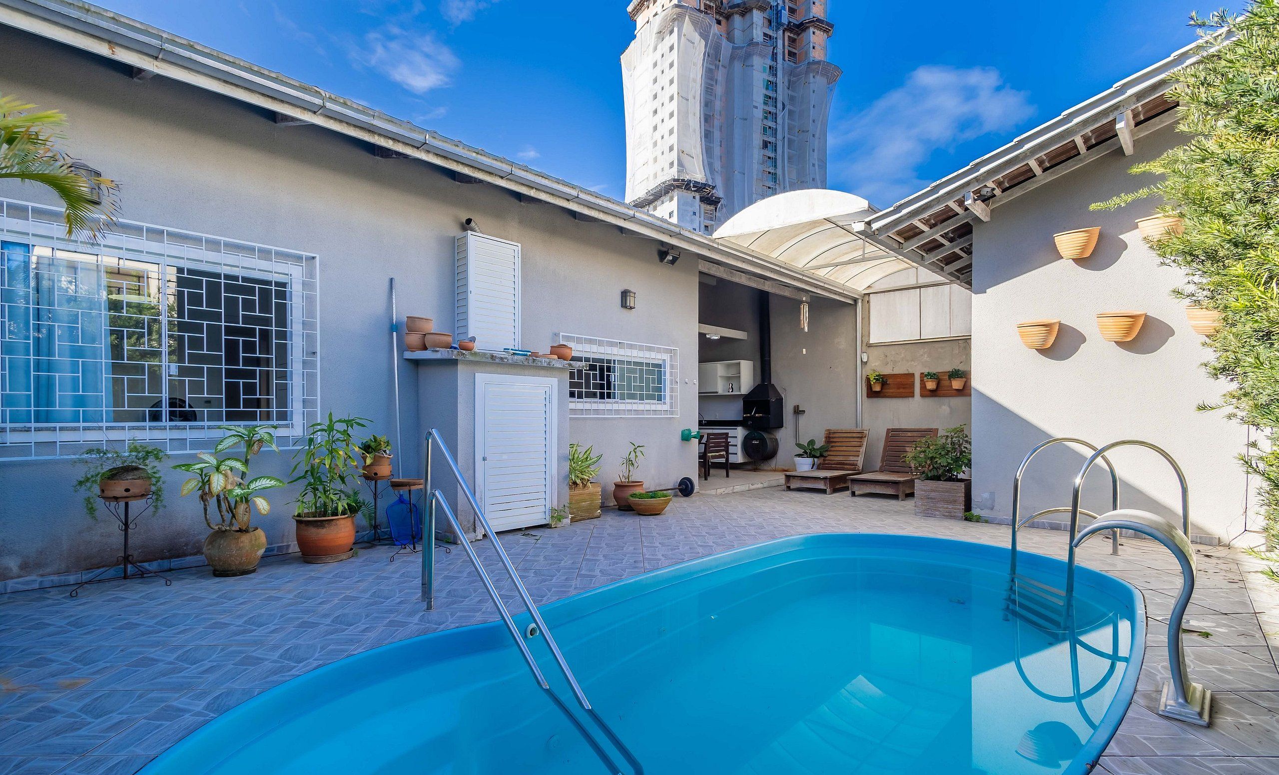 A swimming pool with a ladder, surrounded by potted plants and outdoor furniture.