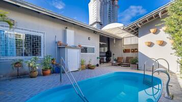 A swimming pool with a ladder, surrounded by potted plants and outdoor furniture.