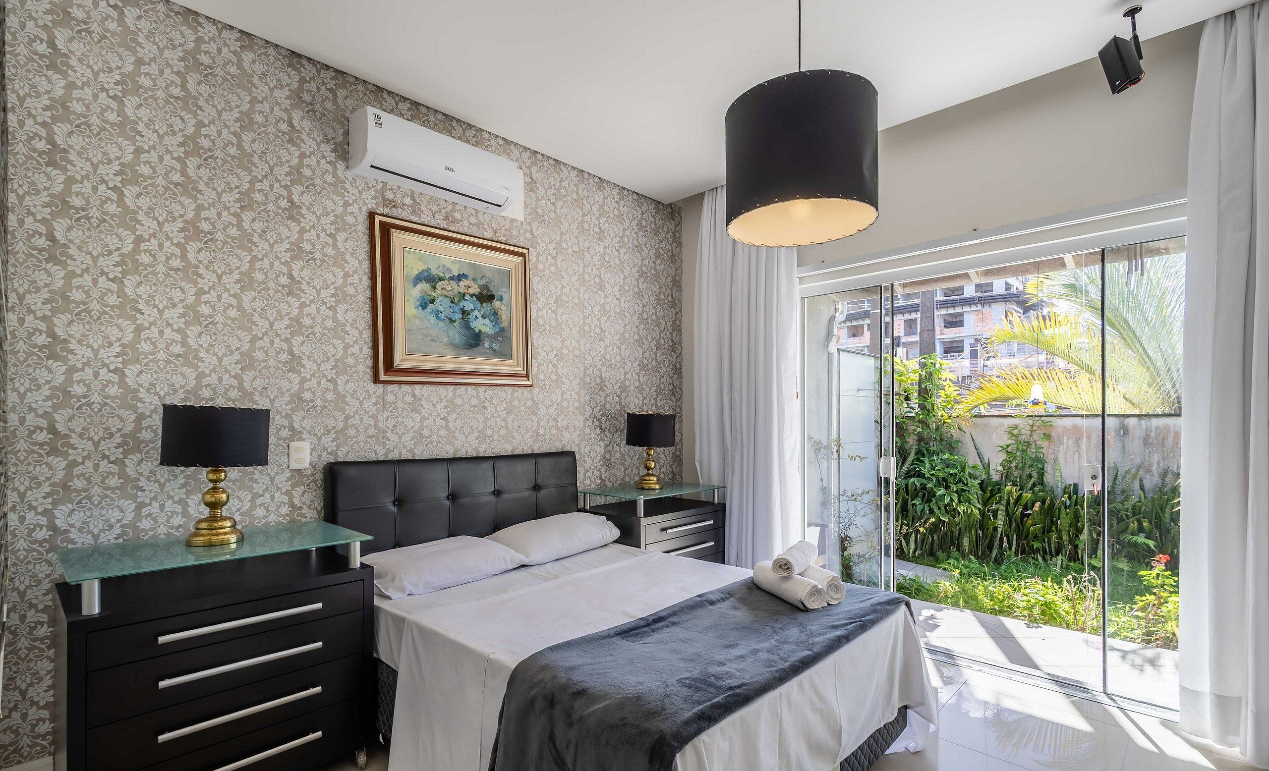 A bedroom with a bed, bedside tables, a painting, and a view of greenery outside.
