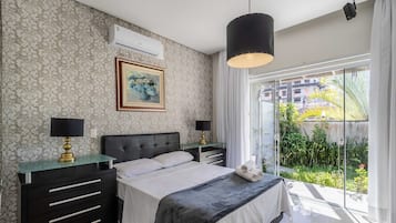 A bedroom with a bed, bedside tables, a painting, and a view of greenery outside.