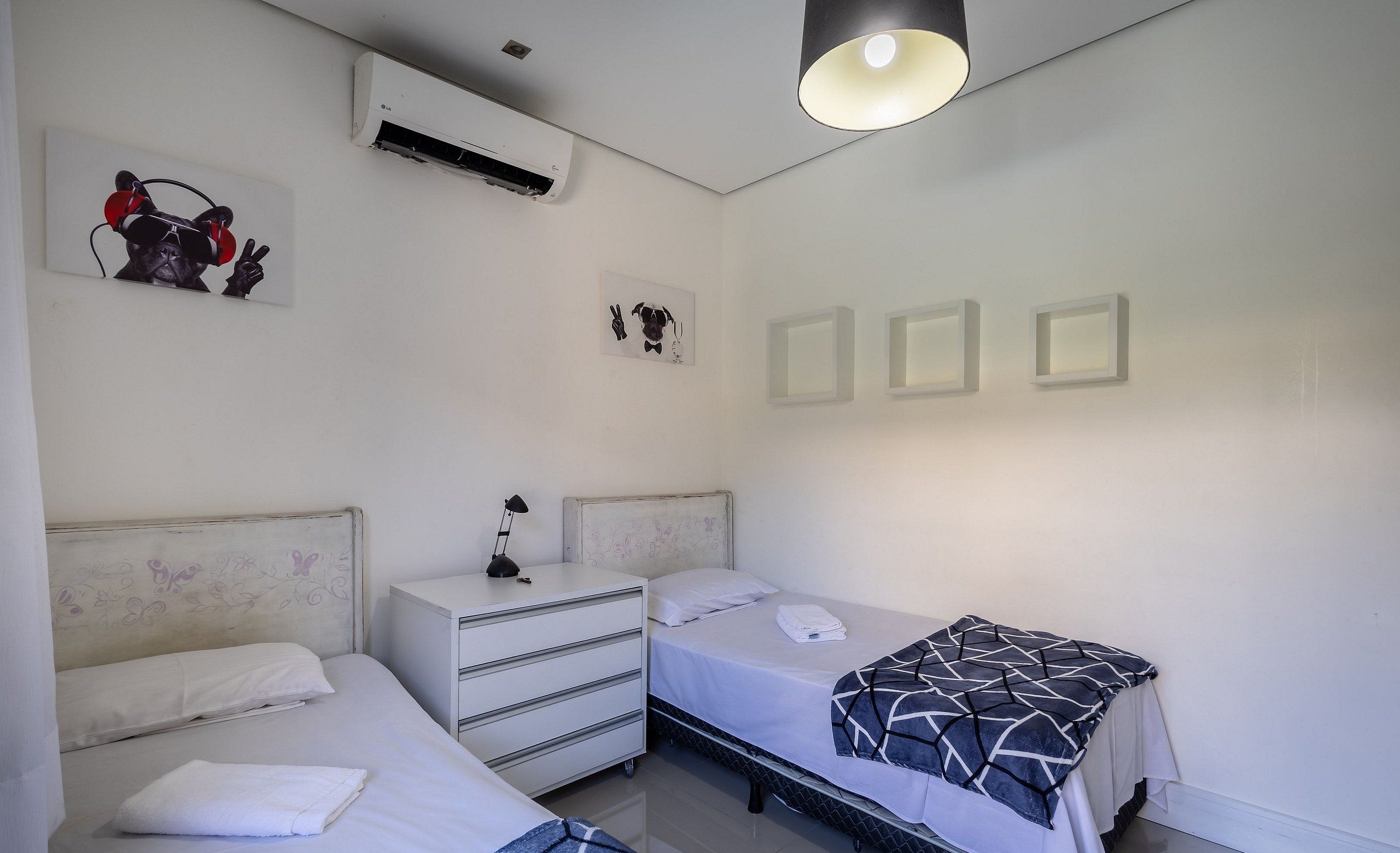 Un dormitorio con dos camas, una mesita de noche con lámpara y aire acondicionado instalado en la pared.