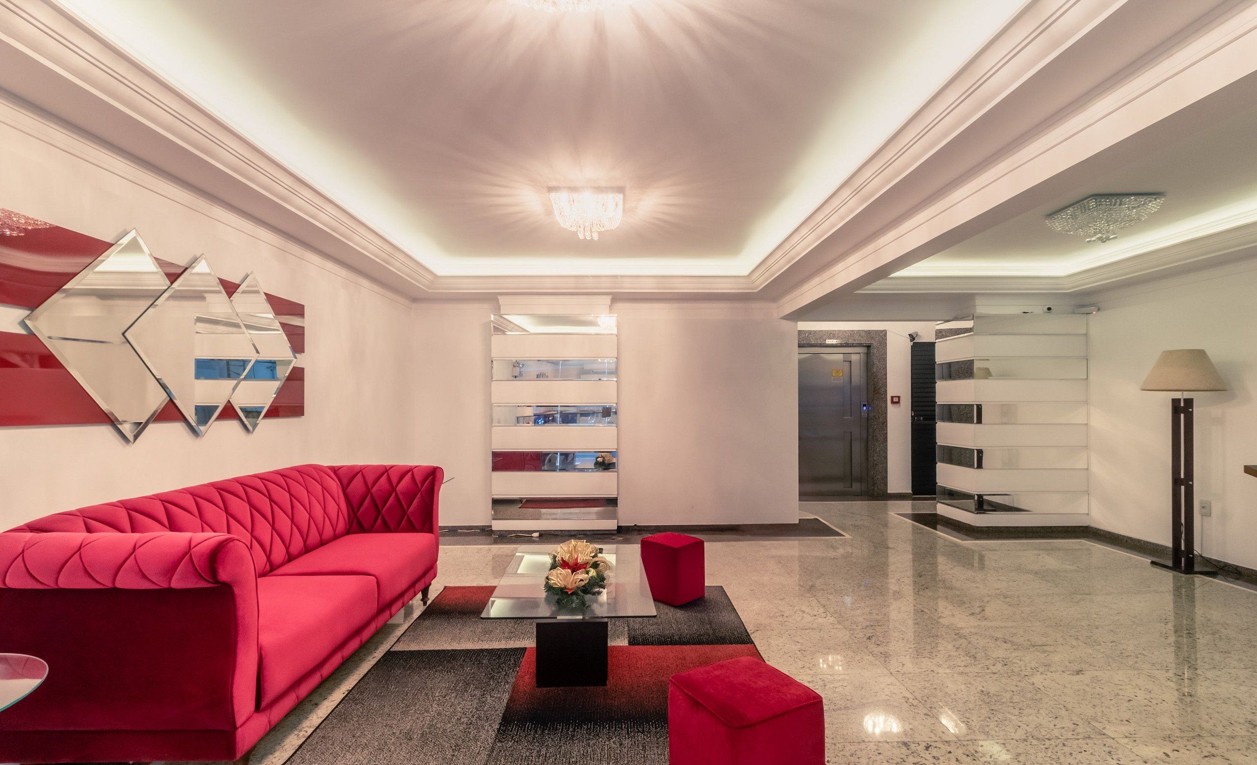 A modern lobby with a red sofa, a glass coffee table, and a chandelier.