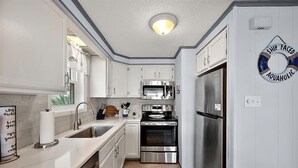 Una cocina compacta con armarios blancos, electrodomésticos de acero inoxidable y suelo de madera.