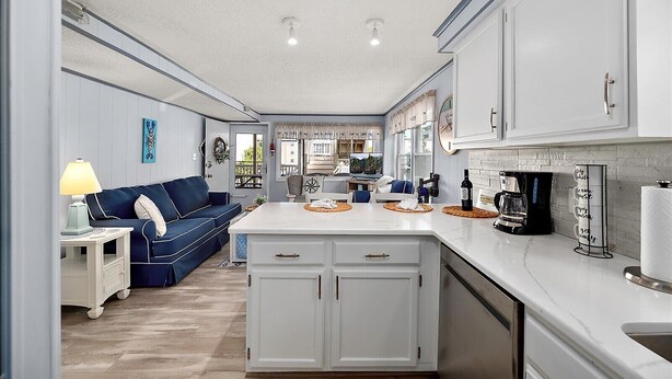 Una cocina moderna con armarios blancos, una isla central y una zona de comedor con un sofá azul.