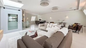 A modern living room with a large sectional sofa, a glass door leading to a balcony, and a dining area in the background. - CLASSIC LONDON ARCHITECTURE IN THE MOST DESIRABLE NEIGHBORHOODS—BAYSWATER (London)