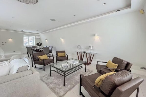 A modern living room with a sofa, two armchairs, a coffee table, and a dining area with a glass table and chairs.