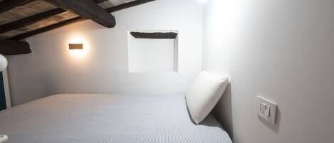 A bedroom with a bed, a wall-mounted light, and a wooden beam ceiling.