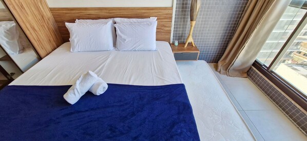 A hotel room with a neatly made bed, a blue blanket, and a wooden headboard. - COBAR0138 - Edifício Barra Premium (Salvador)