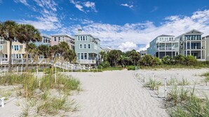 A beachfront property with a sandy beach, a white fence, and a row of colorful houses with balconies. - Stay @ The Grand in Wild Dunes (Isle Of Palms)