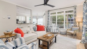 A spacious living room with a white sofa, striped armchairs, a wooden coffee table, and a ceiling fan. - Stay @ The Grand in Wild Dunes (Isle Of Palms)