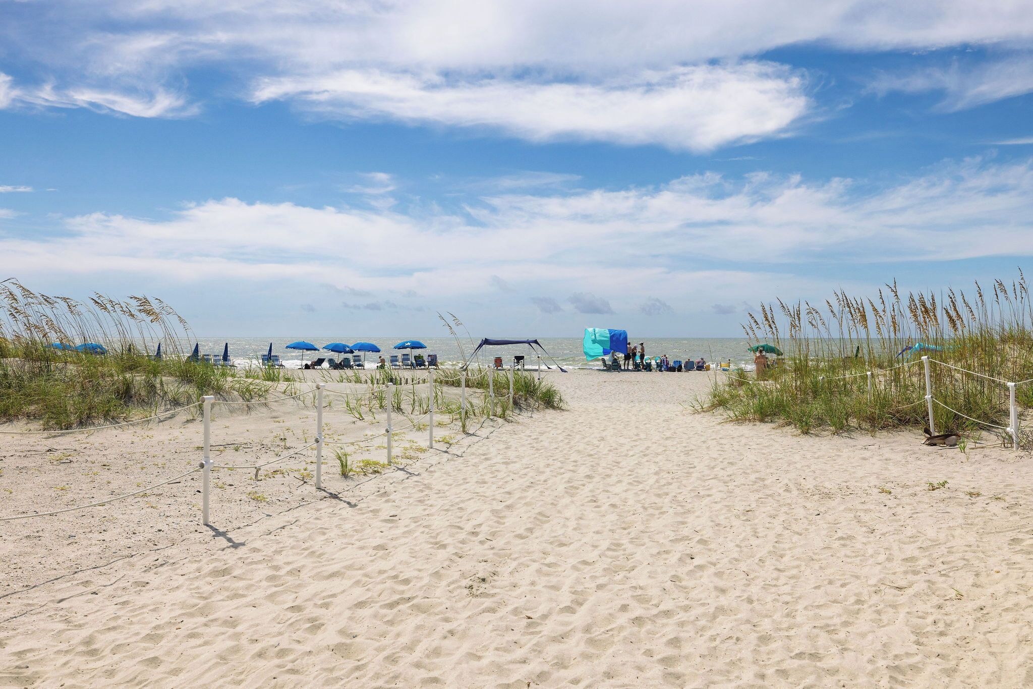 A sandy beach path leading to beach umbrellas and a tent, with a clear sky above.