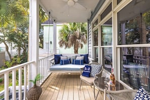A covered porch with a seating area, a table with a bottle, and a view of the surrounding greenery. - Stay @ The Grand in Wild Dunes (Isle Of Palms)