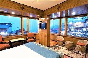 Habitación de hotel con una cama grande, dos sillones, una mesita y un televisor. La habitación tiene ventanas amplias con vistas a un paisaje nevado.