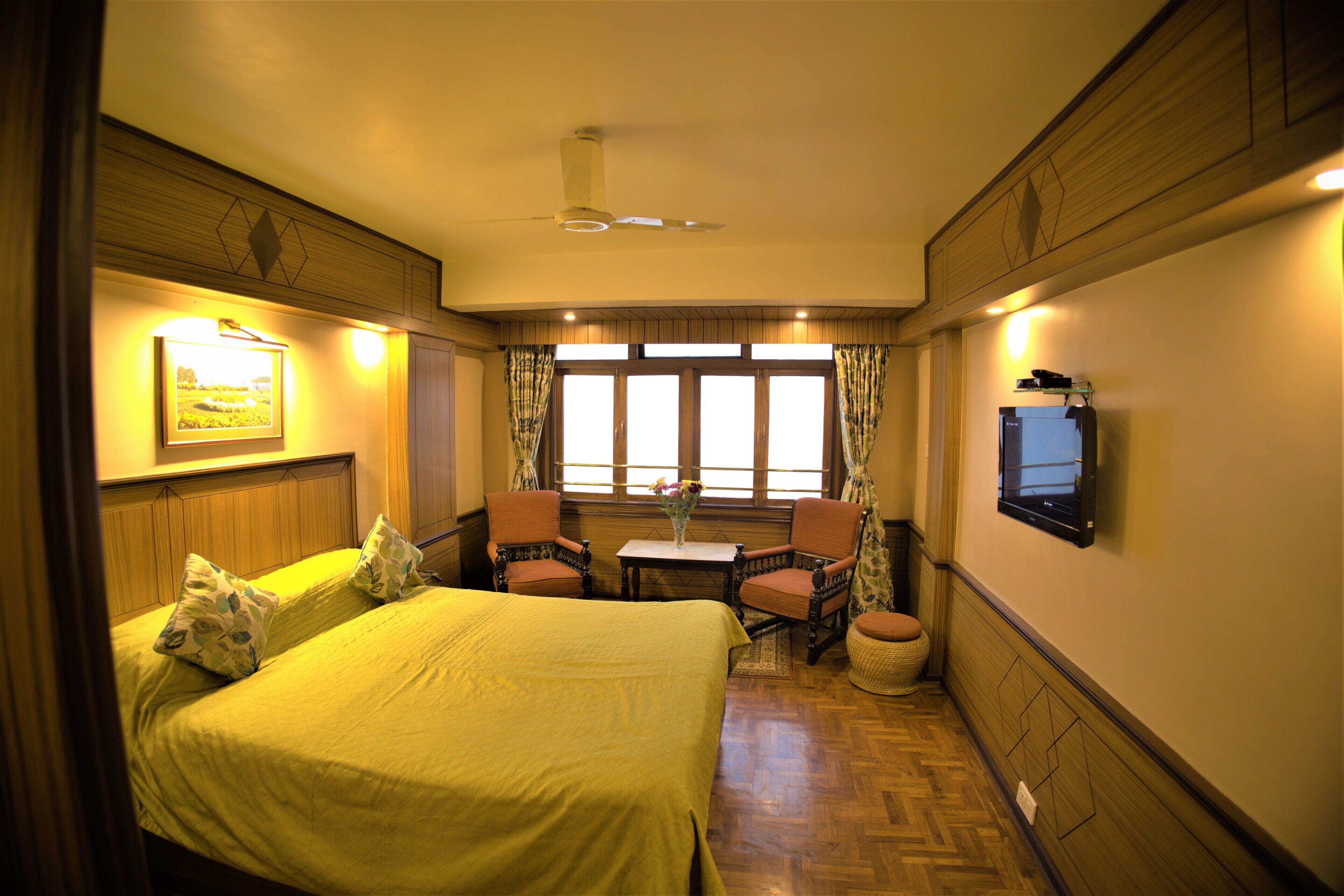 A hotel room with a bed, two chairs, a small table, a television, and a window with curtains.