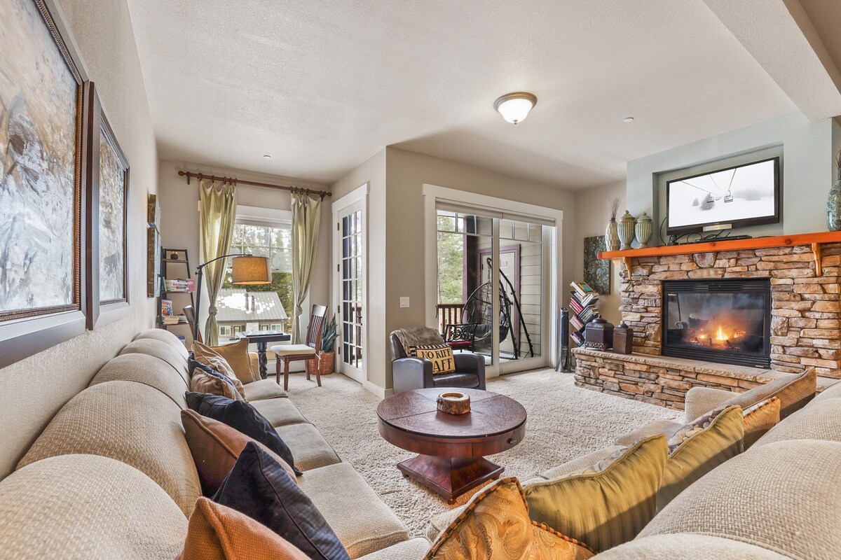 A cozy living room with a fireplace, a large window, and a comfortable seating area.