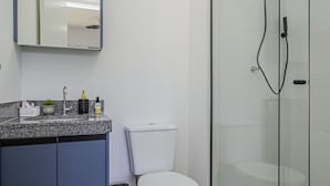 Ein modernes Badezimmer mit einer gläsernen Duschkabine, einer weißen Toilette und einer Granitabdeckung mit Spiegel darüber.