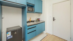 Eine kompakte Küche mit blauen Schränken, einer Mikrowelle, einem kleinen Kühlschrank und einem Waschbecken.