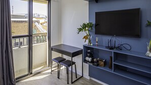 Ein modernes Zimmer mit großem Fenster, Schreibtisch, Stuhl, einem Flachbildfernseher an einer blauen Wand und einer kleinen Pflanze auf dem Schreibtisch.