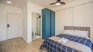 Ein Schlafzimmer mit einem Bett, einem Deckenventilator, einer Tür und einem durch eine offene Tür einsehbaren Badezimmer.