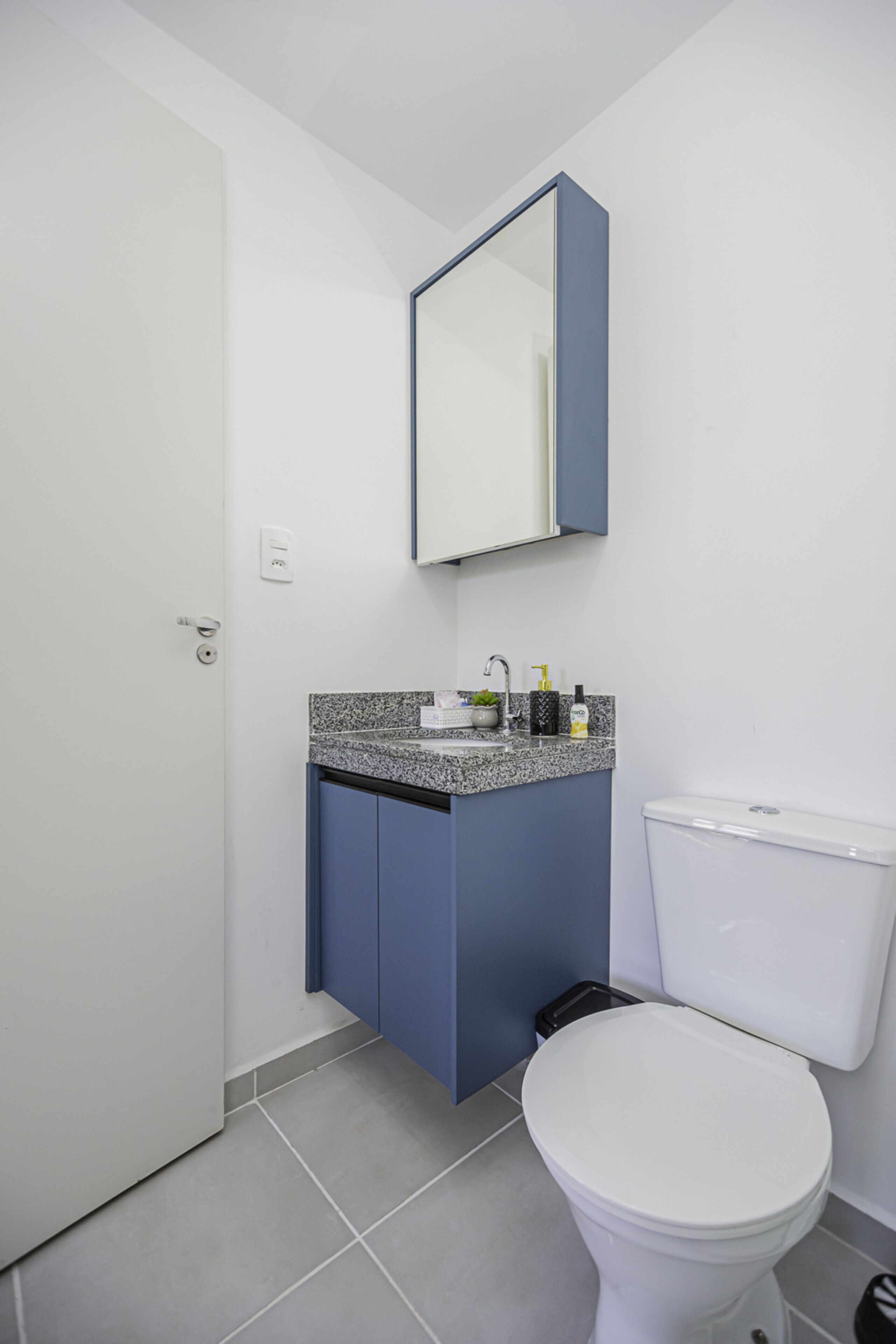 A modern bathroom with a white toilet, a blue cabinet, a granite countertop, and a mirror above the sink.