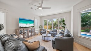 Un salón amplio con una gran televisión de pantalla plana, sofás de cuero, una mesa de centro y un ventilador de techo.