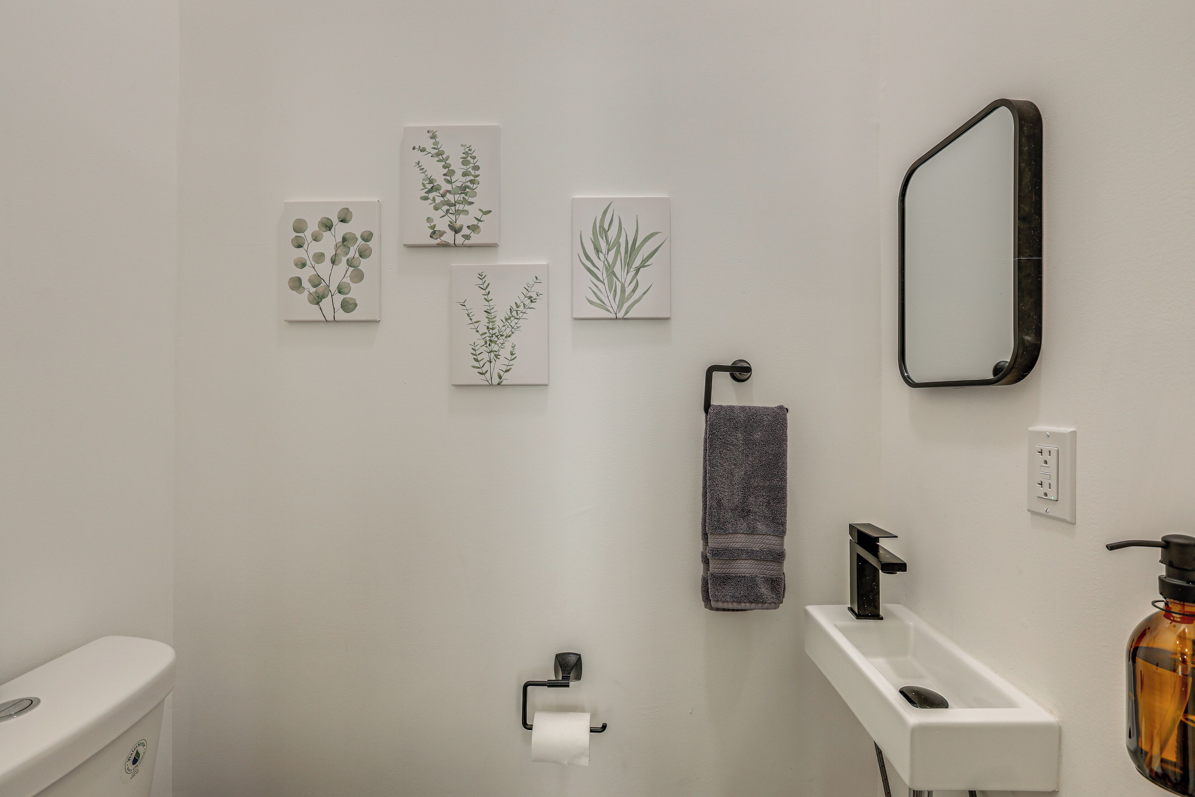 A bathroom with a toilet, sink, towel rack, and three framed botanical prints on the wall.