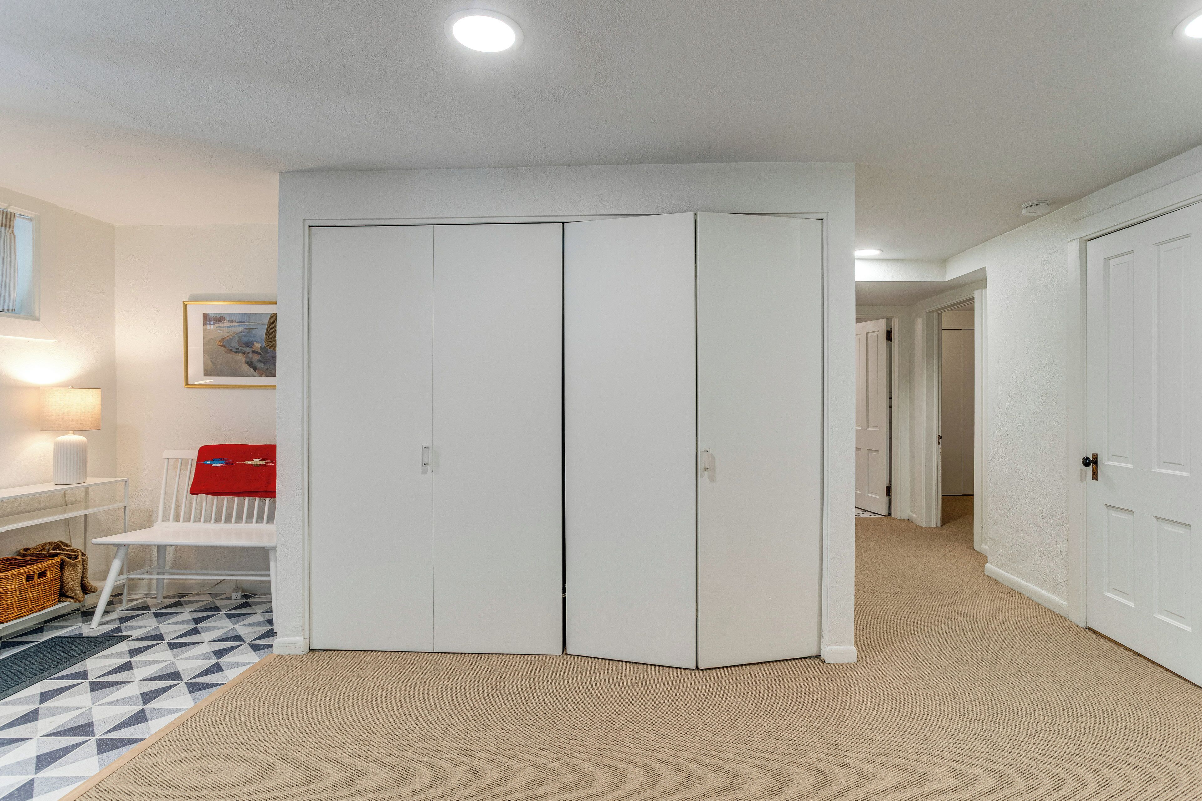 Un pasillo con un armario blanco, una silla blanca, una manta roja y una alfombra estampada.