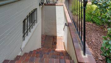 A narrow stairway with red brick steps leading to a white wall with a window and a black metal railing.