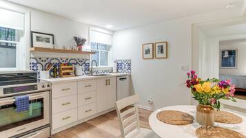 Una cocina moderna con armarios blancos, horno empotrado y comedor con mesa y sillas blancas.