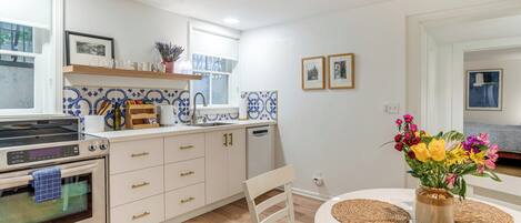 A modern kitchen with white cabinets, a built-in oven, and a dining area with a white table and chairs.