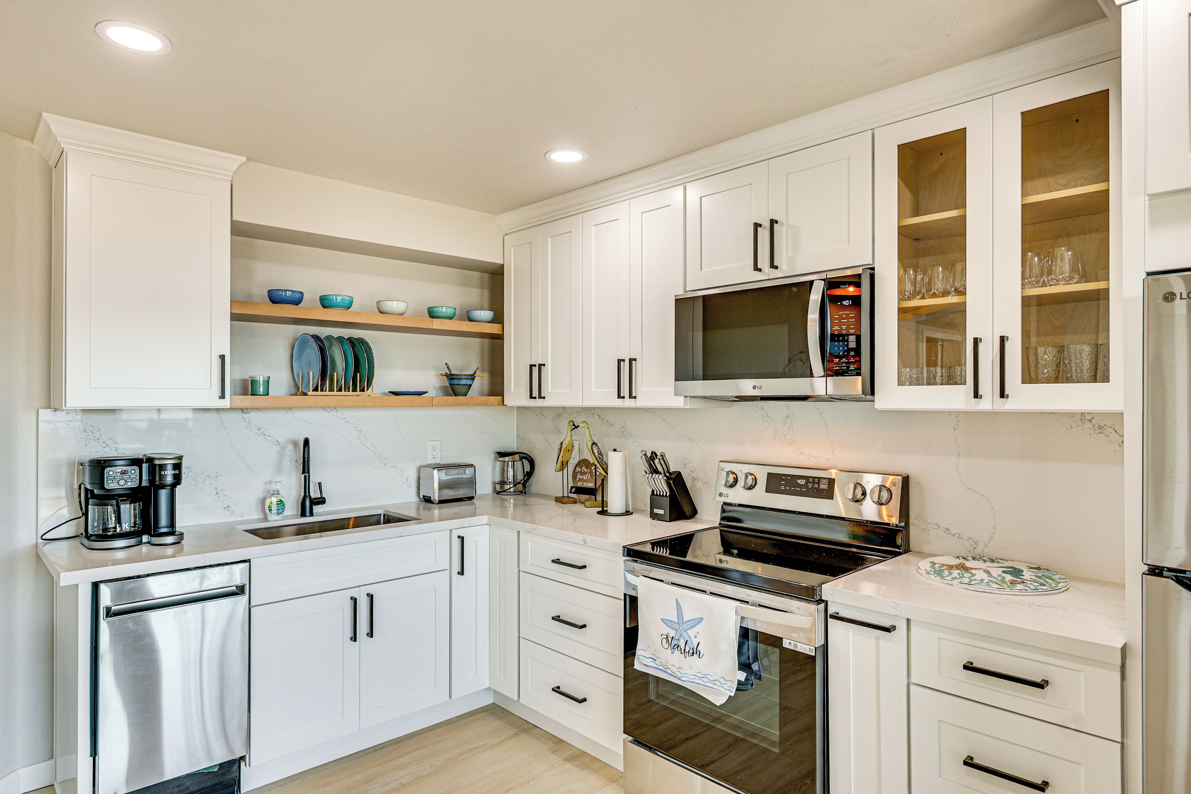 A modern kitchen with white cabinetry, a built-in microwave, an oven, and a coffee maker.