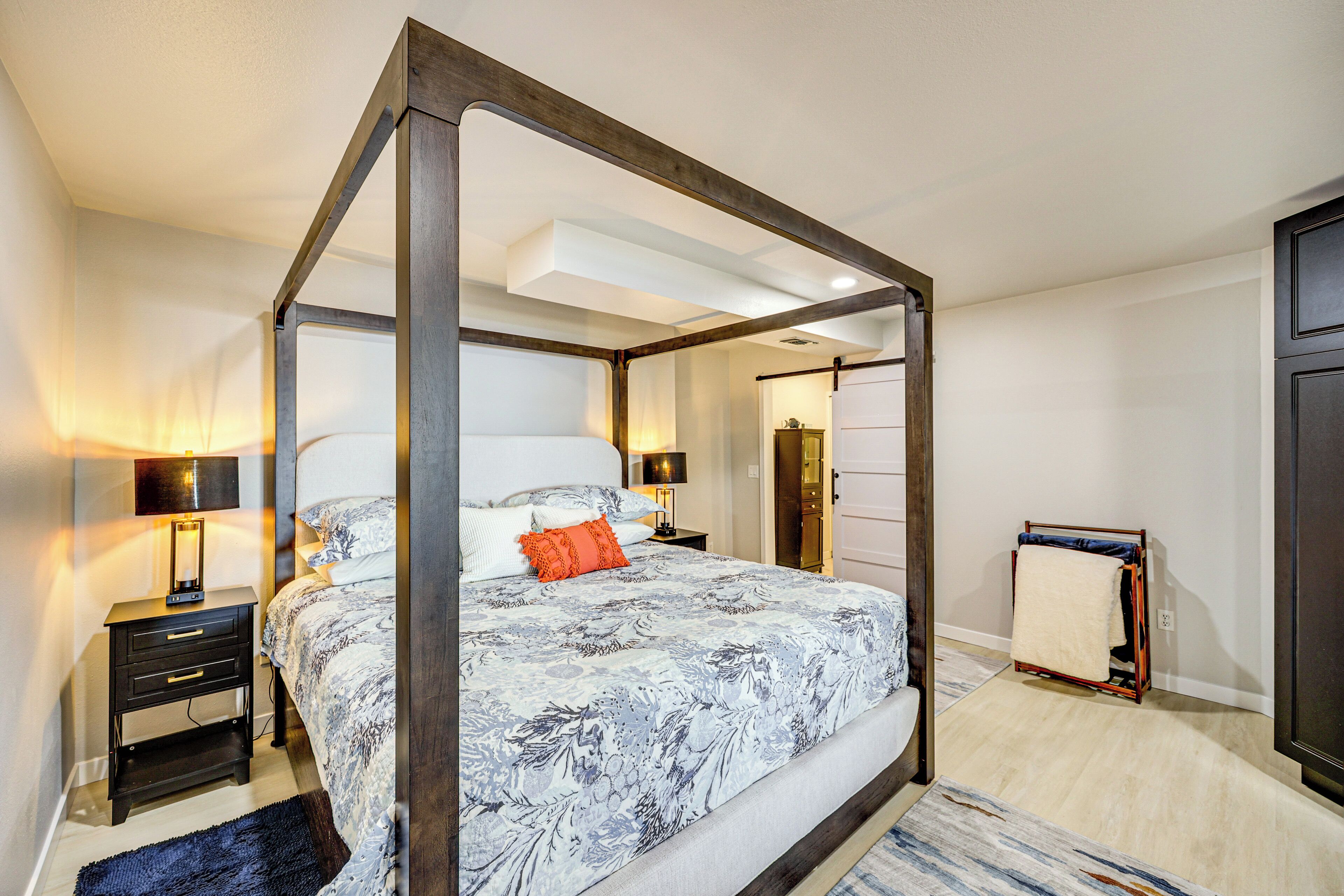 A four-poster bed with a floral bedspread, bedside tables with lamps, and a wooden wardrobe.