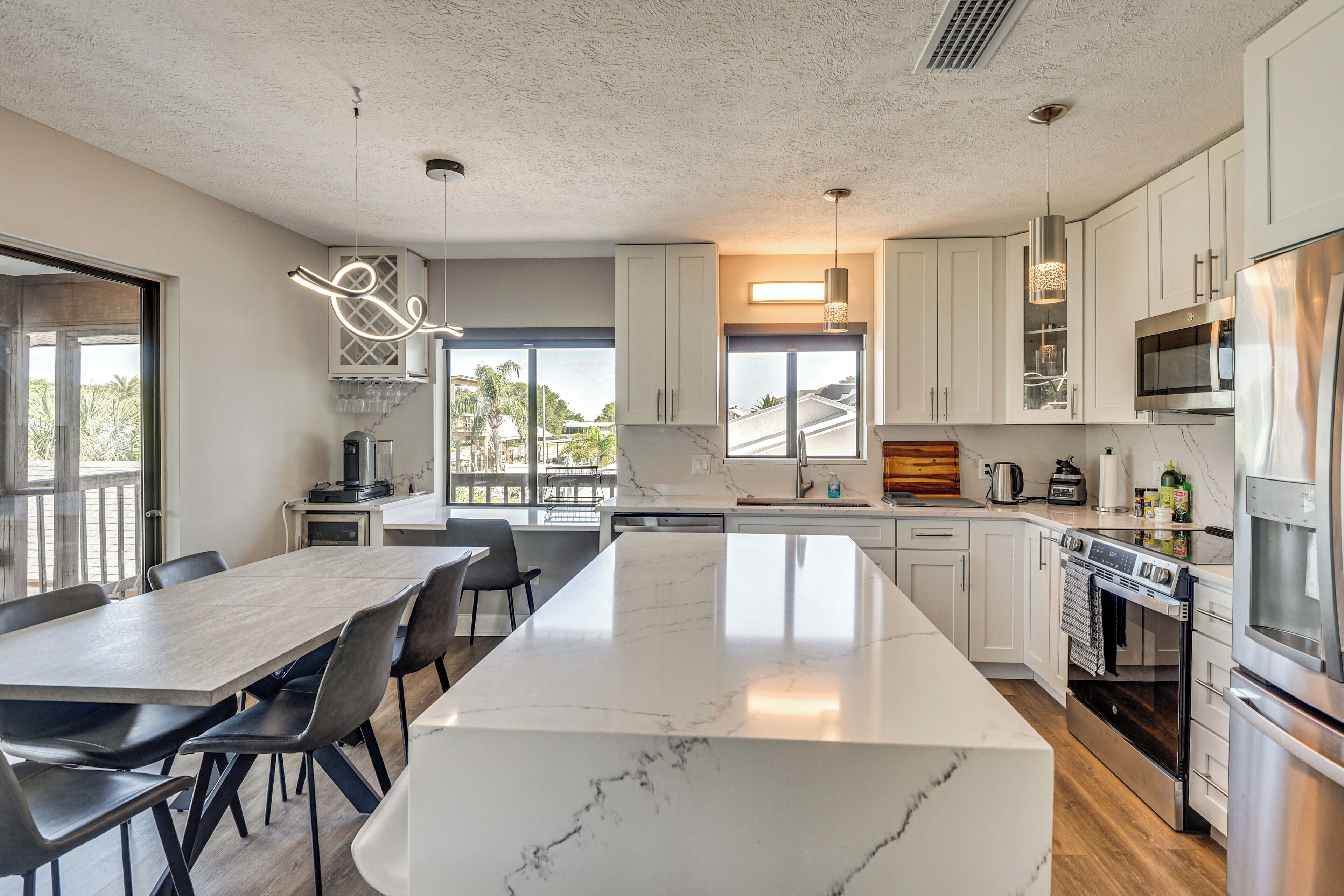 A modern kitchen with a large island, white cabinetry, stainless steel appliances, and a view of the outdoors.
