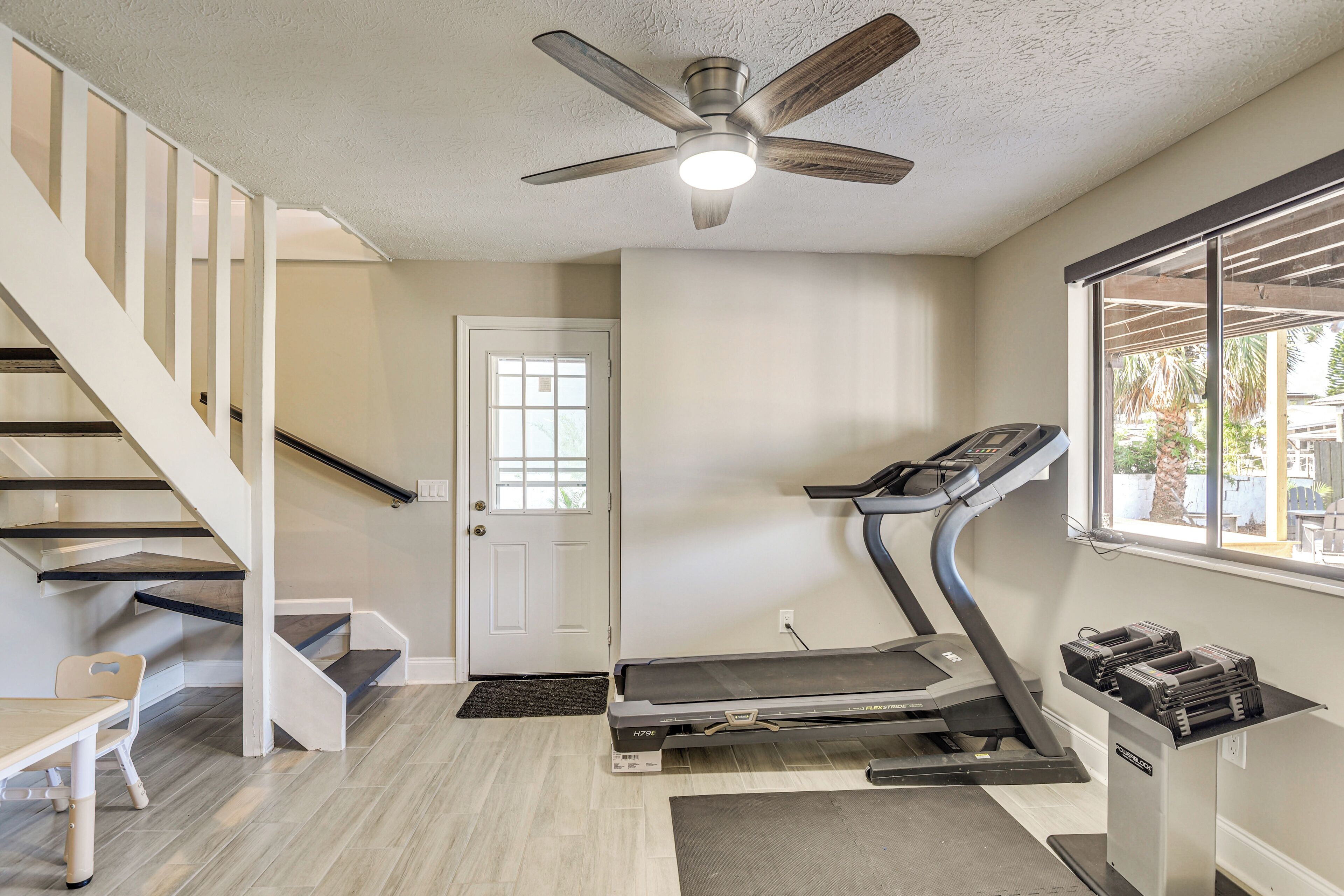 A home interior with a staircase, a door, a ceiling fan, a treadmill, and a window.