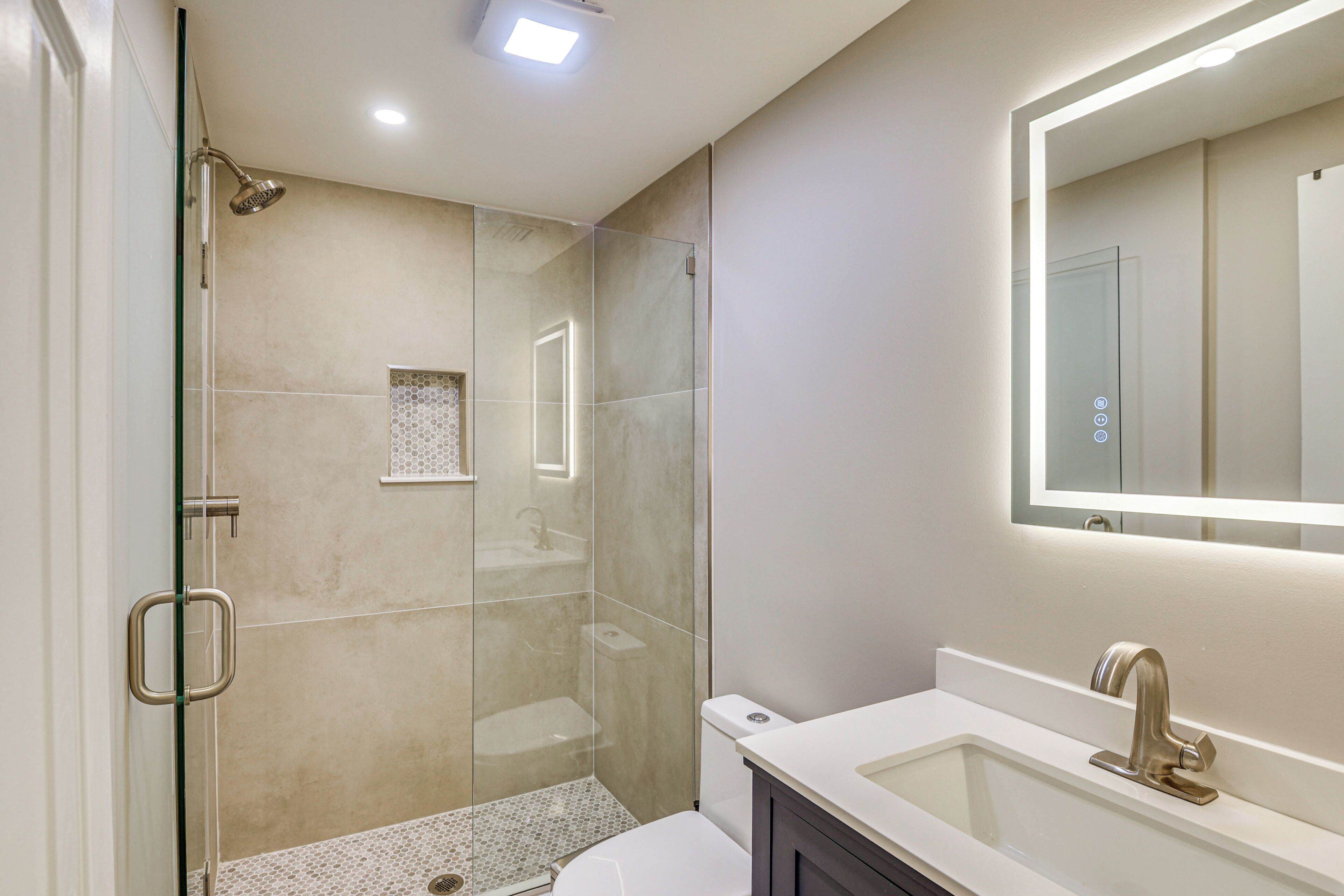 Ein modernes Badezimmer mit einer gläsernen Dusche, einem weißen Waschbecken mit Goldarmatur und einem großen Spiegel darüber.
