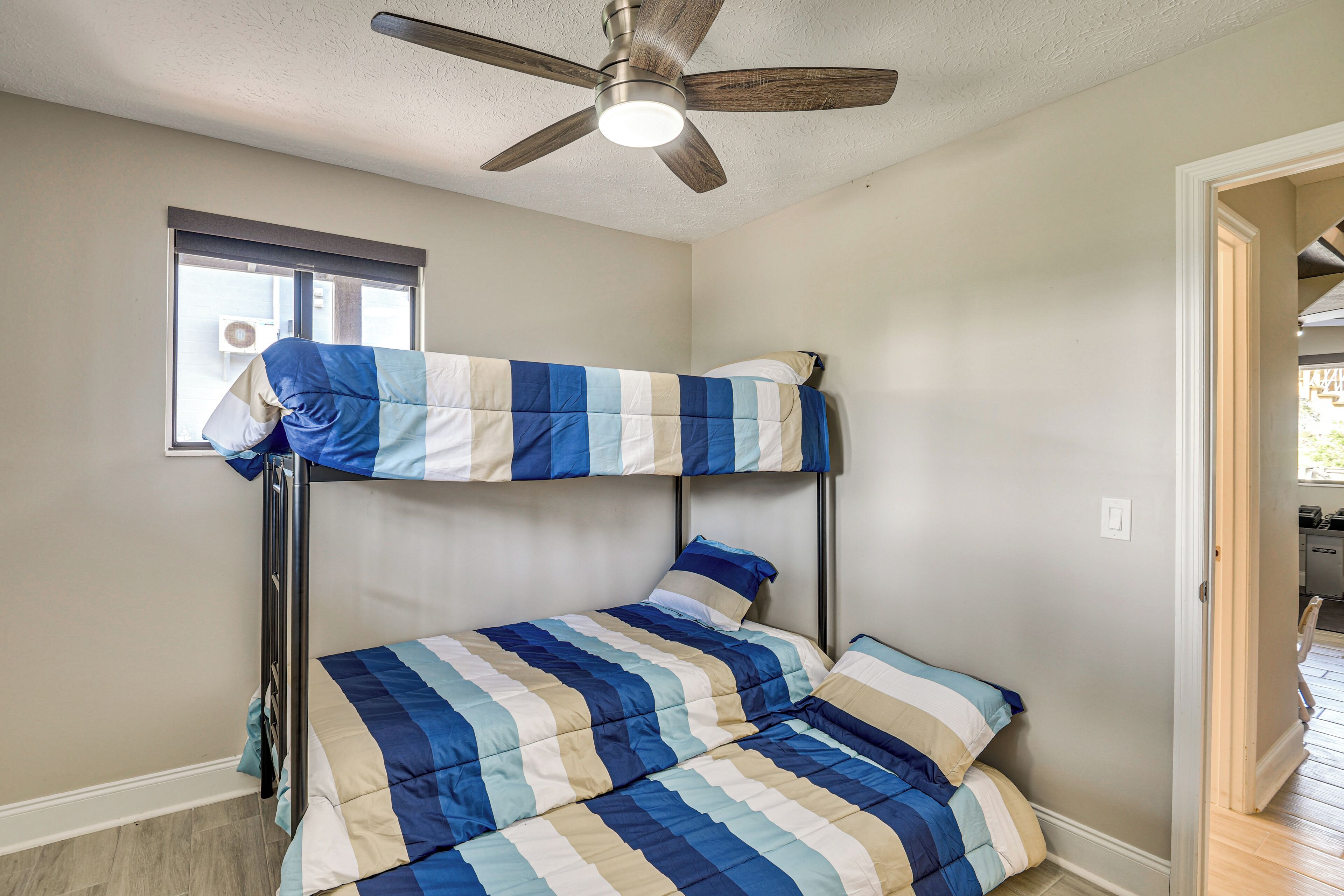 A bunk bed with a striped blue and white bedding, a ceiling fan, and a window with blinds.