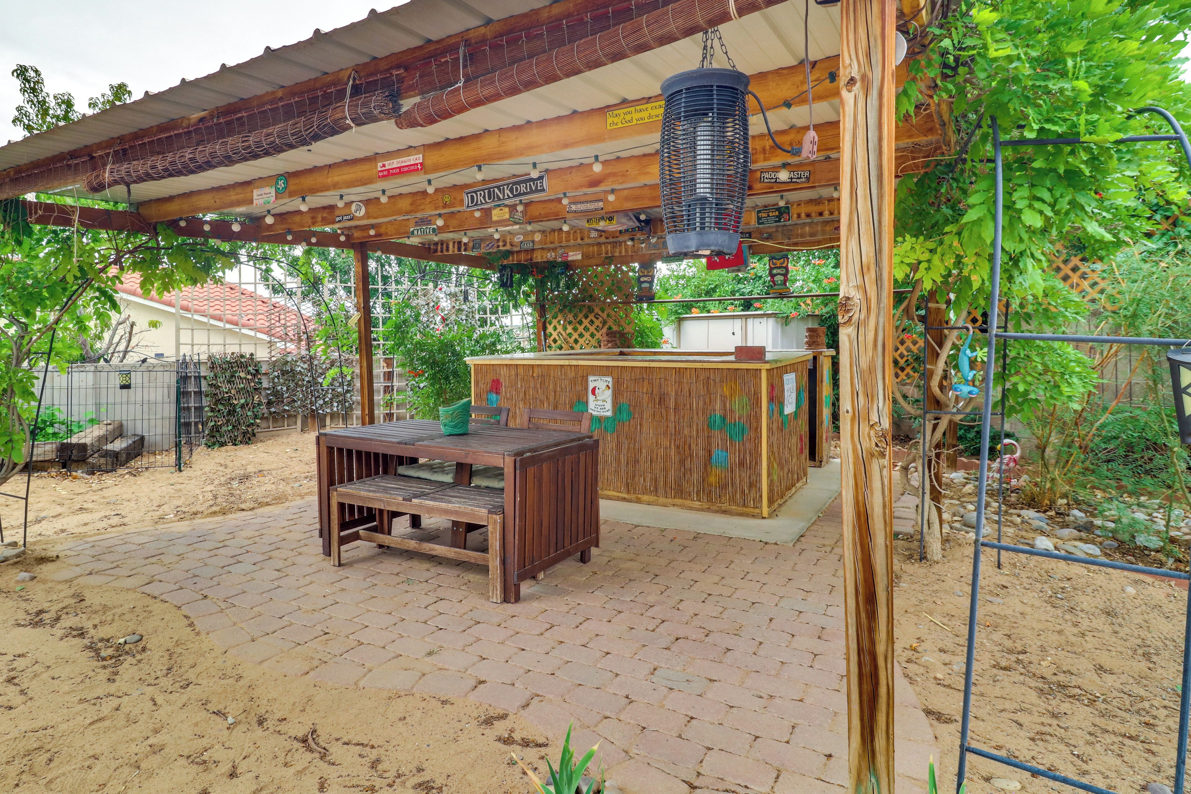 An outdoor seating area with a wooden table and chairs, a hanging basket, and a covered structure with various signs.