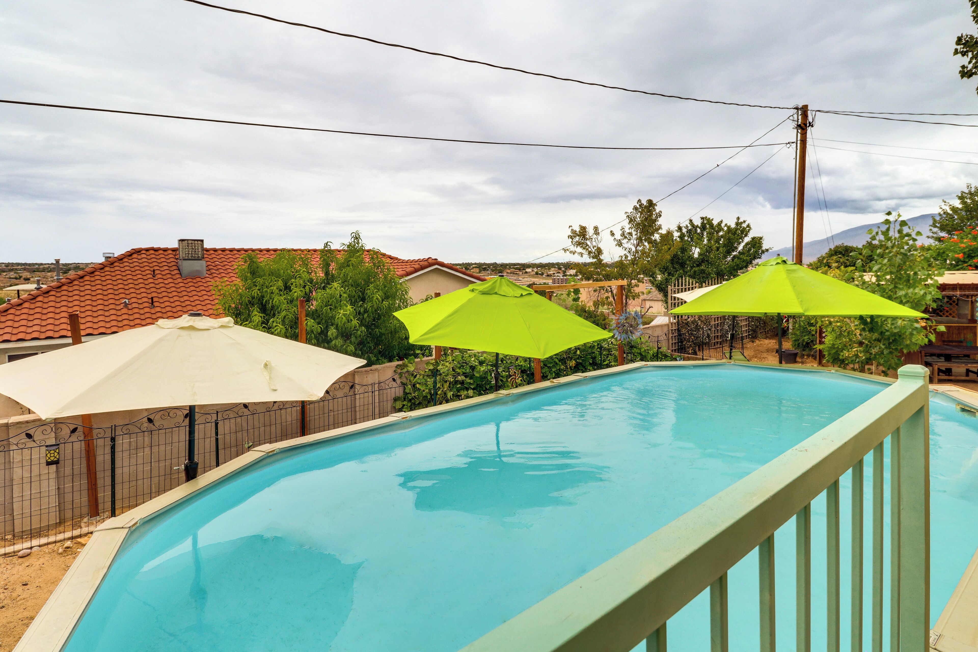 A swimming pool with a wooden deck and a metal fence. There are two umbrellas providing shade.