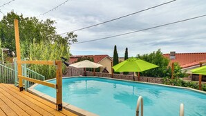 A wooden deck with a swimming pool, surrounded by greenery and buildings with red roofs. - Outdoor Bar & Large Pool: Retro ABQ Retreat! (Albuquerque)