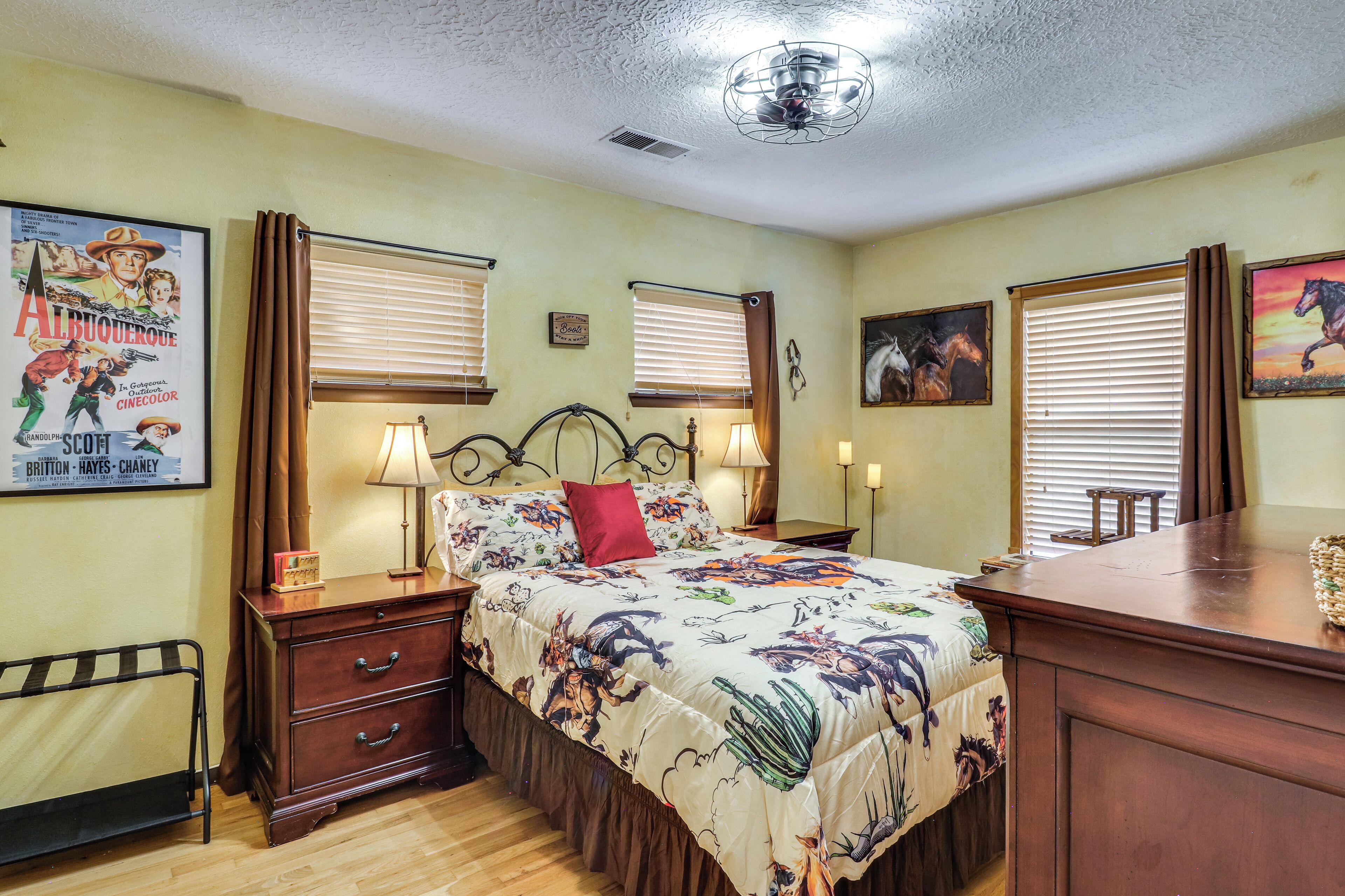 A bedroom with a bed, two bedside tables with lamps, a dresser, a ceiling fan, and a poster on the wall.
